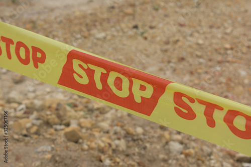 Red and yellow stop warning tape. Tape says stop. Brown gravel backgroung photo