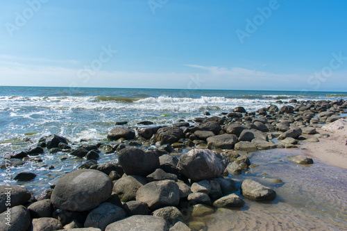 Landscape of beach covered in stones. Blue water. Cloudy sky background.
