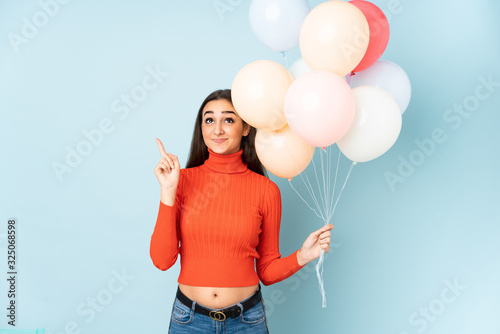 Young woman catching many balloons isolated on blue background pointing with the index finger a great idea © luismolinero