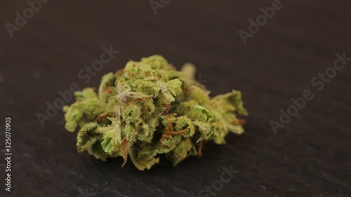 Macro shot of sativa or indica weed bud with fresh trichoma crystals on turning slate board table. Black background