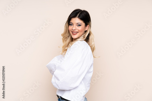 Teenager girl isolated on beige background with arms crossed and happy