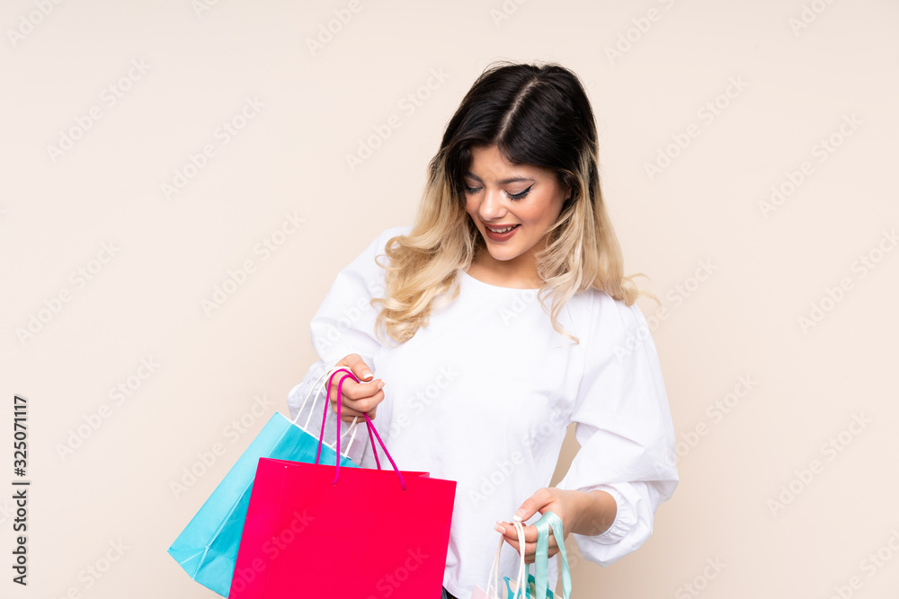 Teenager girl isolated on beige background holding shopping bags and looking inside it