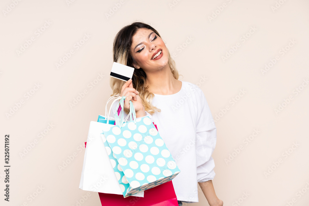 Teenager girl isolated on beige background holding shopping bags and a credit card Teenager girl isolated on beige background holding shopping bags and a credit card