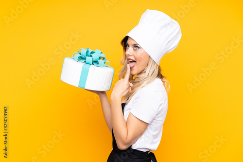 Teenager girl pastry holding a big cake isolated on yellow background