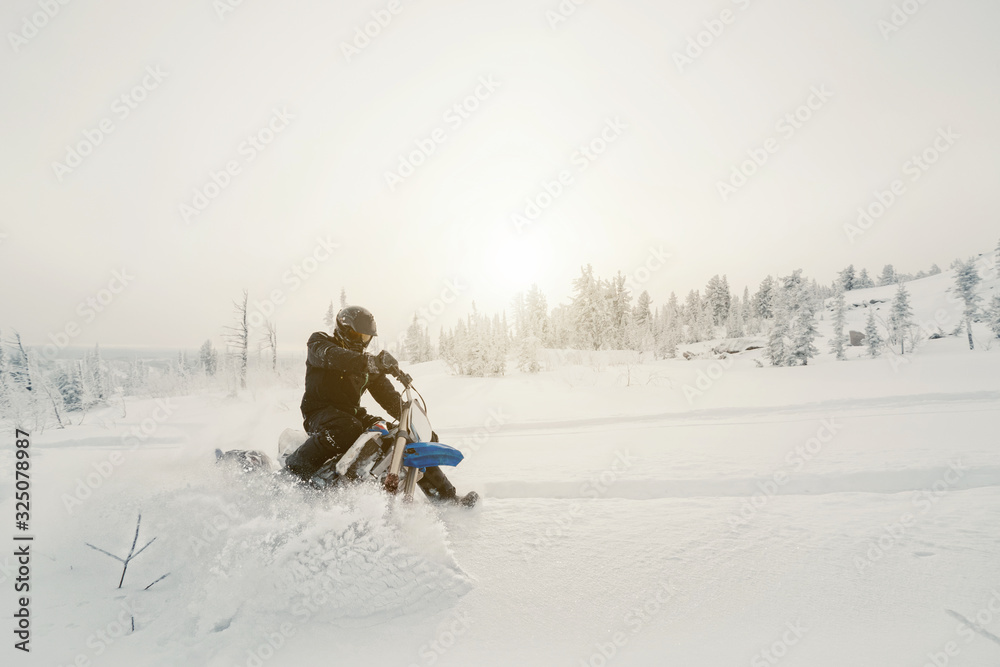 Rider with snowbike on snow covered mountain slop. Sunny fog, outdoor activity in winter day