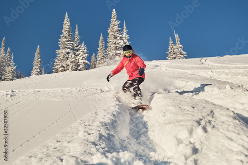 Female snowboarder wearing hoodie riding on mountain slop in big snow powder. Sunny winter day in ski resort photo