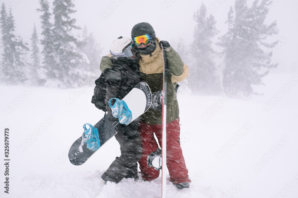 Love couple of snowboarders outdoors in beautiful winter landscape under snow covered spruce trees, blizzard and heavy snow in winter day Love couple of snowboarders outdoors in beautiful winter landscape under snow covered spruce trees, blizzard and heavy snow in winter day