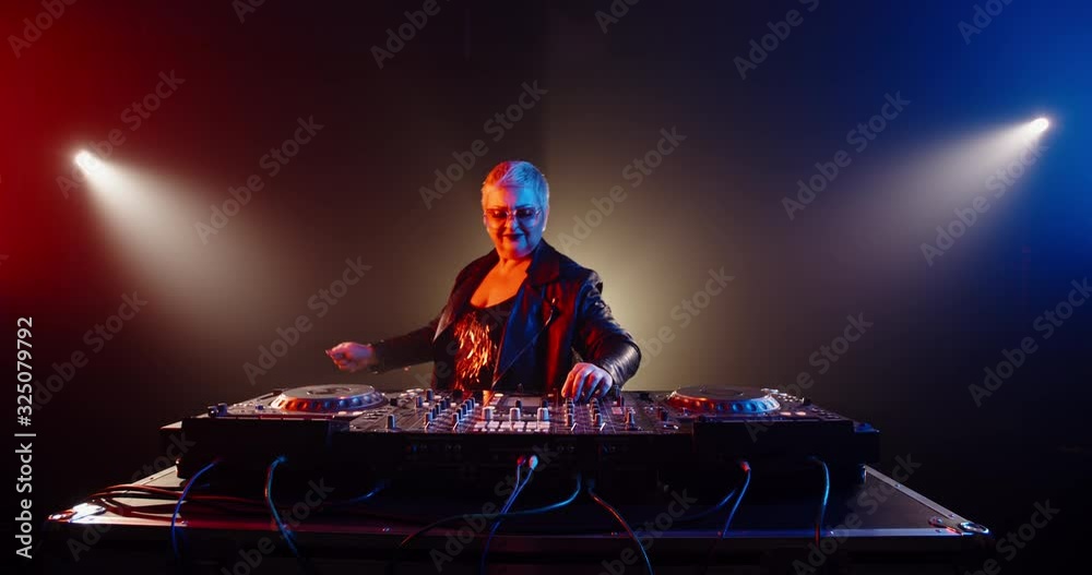 Funny caucasian grandma in authentic outfit and makeup working as a cool dj in a nightclub, dancing and cheering at turntables 4k footage Funny caucasian grandma in authentic outfit and makeup working as a cool dj in a nightclub, dancing and cheering at turntables 4k footage