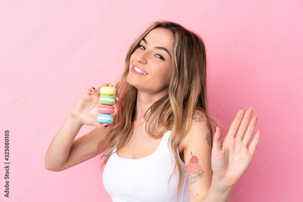 Young woman with macarons over isolated pink background saluting with hand with happy expression Young woman with macarons over isolated pink background saluting with hand with happy expression