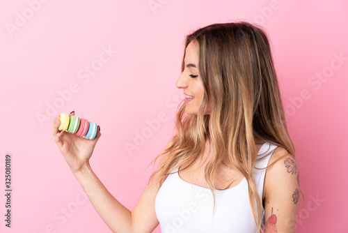Young woman with macarons over isolated pink background with happy expression