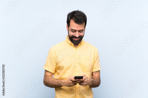 Young man with beard over isolated blue background sending a message with the mobile