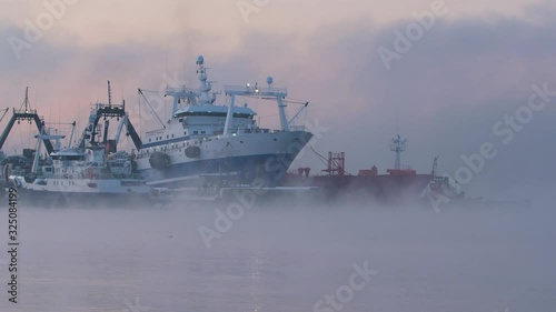 Fishing boats in the early morning at sunrise are in the port in a thick fog photo