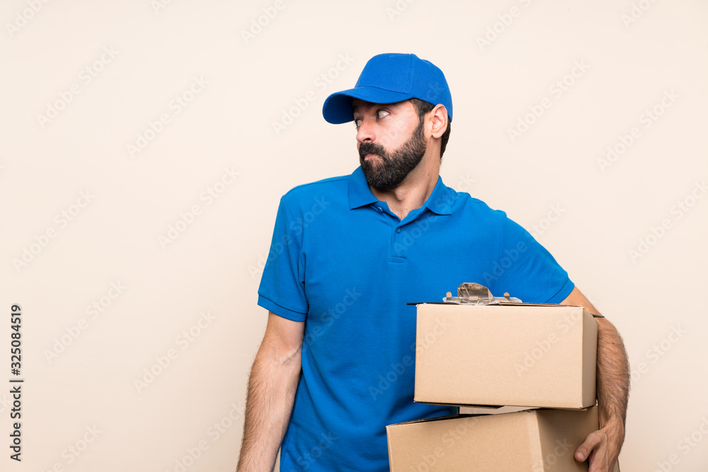 Delivery man with beard over isolated background making doubts gesture looking side Delivery man with beard over isolated background making doubts gesture looking side