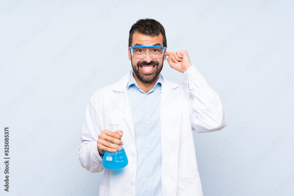 Young scientific holding laboratory flask over isolated background frustrated and covering ears Young scientific holding laboratory flask over isolated background frustrated and covering ears
