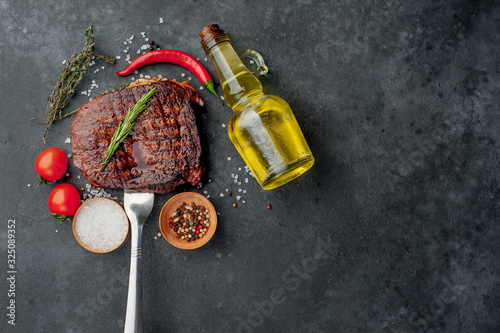 Beef steak on a fork on a stone background with spices with copy space for your text.
