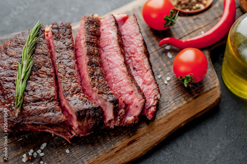 Grilled beef steak on a cutting board with spices and tomatoes on a stone background