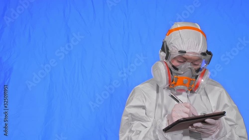 Scientist virologist in respirator makes write in an tablet computer with stylus. Woman wearing protective medical mask. Concept health safety virus coronavirus epidemic 2019 nCoV. Chroma key blue. photo