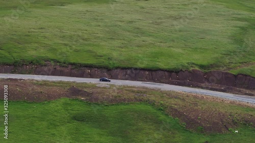 Black sedan car on sharp turn driving alone asphalt winding zig zag empty serpentine road and mid shot famous Caucasus Dzhily Su freeway at summer cloudy day - Aerial drone view photo