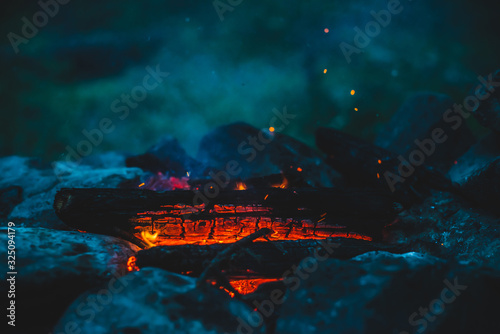 Vivid smoldered firewoods burned in fire close-up. Atmospheric warm background with orange flame of campfire and blue smoke. Unimaginable full frame image of bonfire. Burning logs in beautiful fire. © Daniil