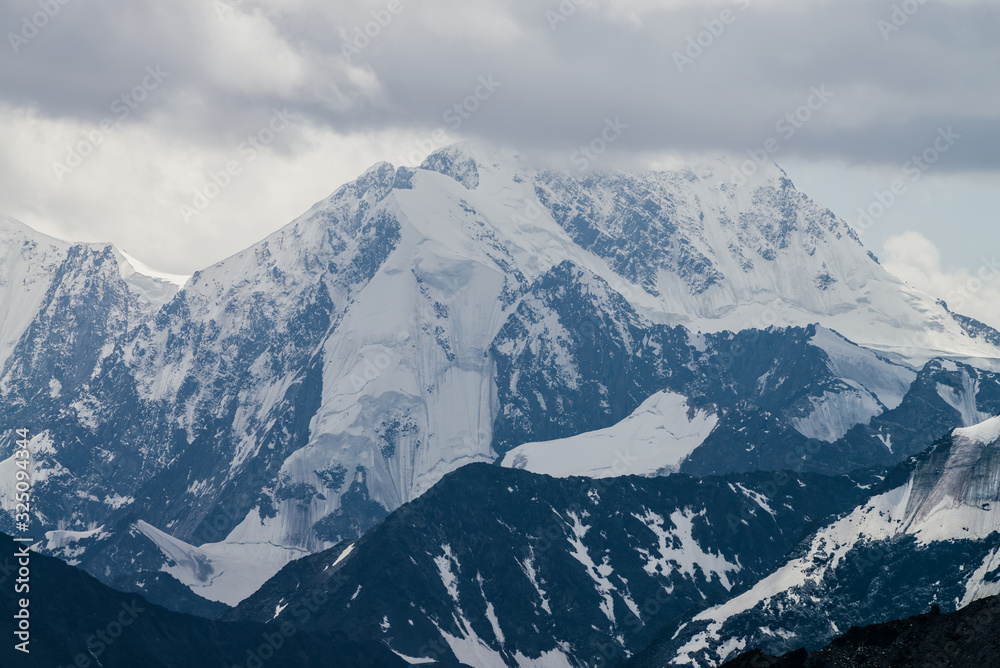 Awesome landscape with huge glacial mountains in bad cloudy weather. Low stormy clouds touch top of snowy mountain with glaciers. Storm is coming due to mountains. Gloomy overcast atmospheric scenery.
