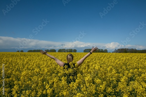 happy woman standing in a yellow canola field with raised arms 