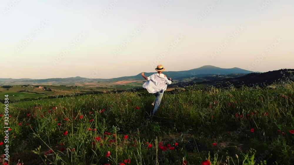 Adventurous female tourist with camera running in slow motion through red poppy meadow during summer vacations in Tuscany countryside, aerial view of carefree young woman wanderlust enjoying nature Adventurous female tourist with camera running in slow motion through red poppy meadow during summer vacations in Tuscany countryside, aerial view of carefree young woman wanderlust enjoying nature
