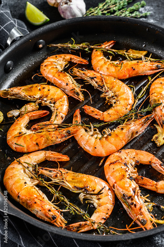 Grilled giant prawns, shrimps with garlic, lemon, spices in pan. Black background. Top view