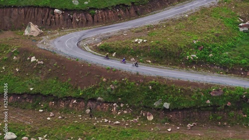 Three motorcyclists on motocross bikes ride on a dangerous serpentine Dzhily Su winding road at summer cloudy day - Aerial drone view photo