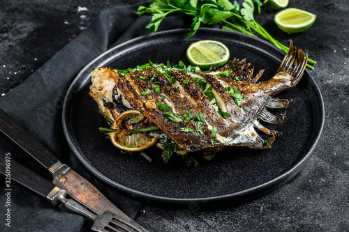 Grilled John Dory fish with lime and parsley in a pan. Black background. Top view