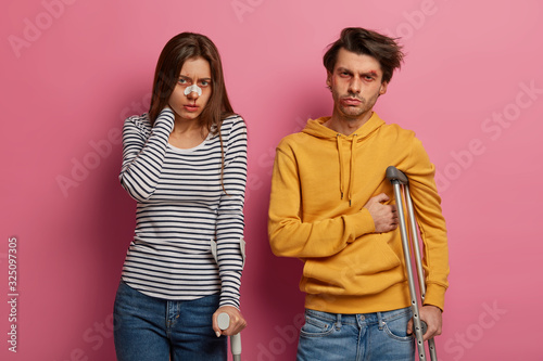 Obraz na plátně Female and male bikers have unlucky race, got into accident because of overspeeding, stand next to each other, use crutches, have leg injuries, limited abilities