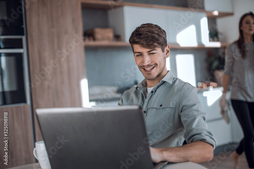 young man sitting in front of open laptop in kitchen