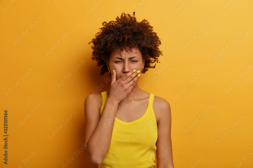 Miserable dejected African American woman cries after breakdown, recalls unhappy memory, covers mouth, wears yellow casual clothes, poses indoor, expresses negative emotions, being under pressure Miserable dejected African American woman cries after breakdown, recalls unhappy memory, covers mouth, wears yellow casual clothes, poses indoor, expresses negative emotions, being under pressure