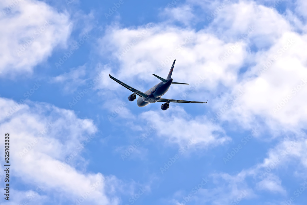 Plane flying in the blue sky amid clouds and sunlight, travel by air