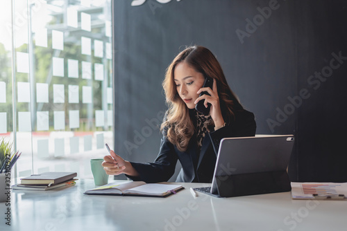 Fotografie Attractive young asian woman talking on the mobile phone and standing at her working place in office
