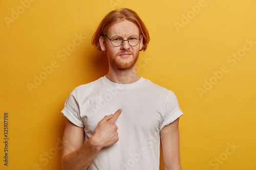 Fotografia Waist up shot of dissatisfied bearded man with ginger bob hairstyle points at hi