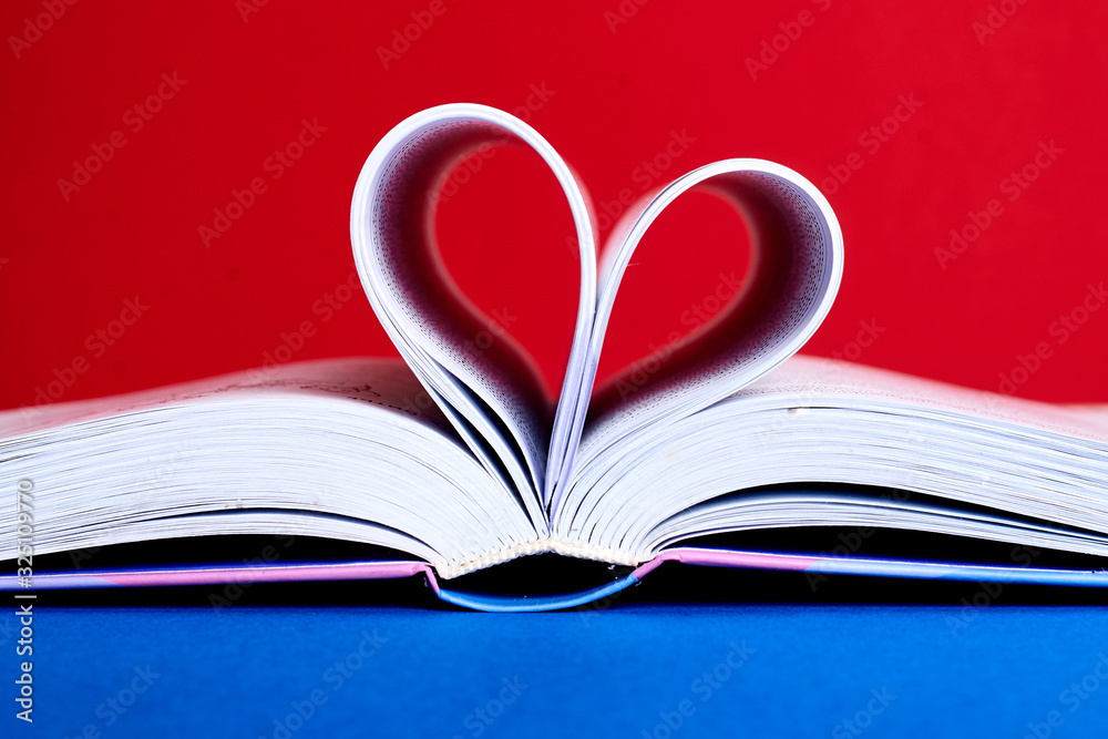 An open book with a folded heart of pages on a red and blue background. An open book with a folded heart of pages on a red and blue background.