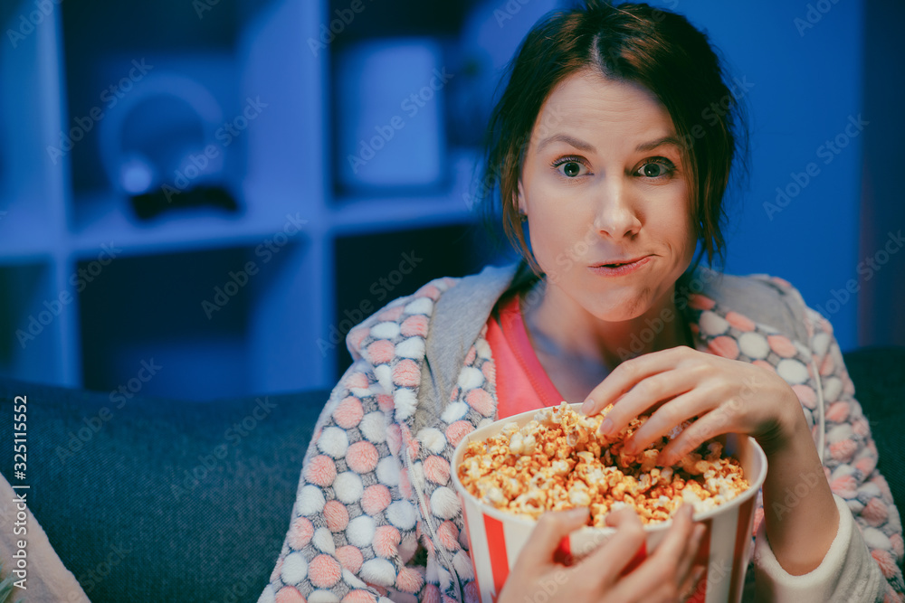 Young lady is watching TV laughing and eating popcorn having fun at home alone enjoying modern television. Youth lifestyle and cheerful people concept Young lady is watching TV laughing and eating popcorn having fun at home alone enjoying modern television. Youth lifestyle and cheerful people concept