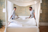 couple smiling, laughing while making bed together in the morning in modern bedroom. couple, togetherness, morning, bedroom, concept.