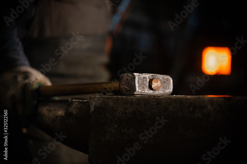 Obraz na plátne A hammer on the anvil in workshop - a man worker standing on the background