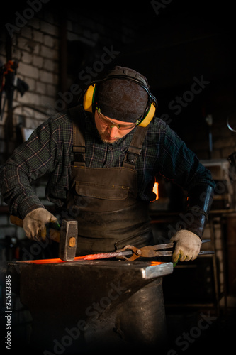 A man in protecting headphones and glasses forging a knife