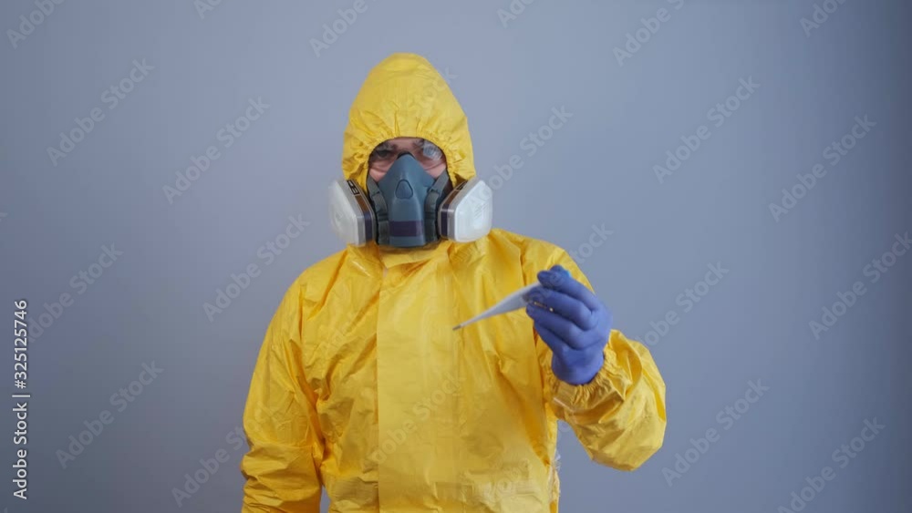A man in a yellow hazmat suit, shows a sign to approach and holds out a thermometer. A man in a yellow hazmat suit, shows a sign to approach and holds out a thermometer.