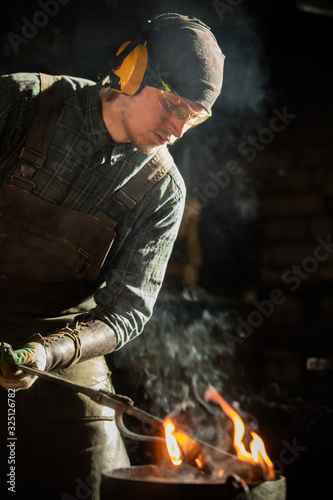 Blacksmith man worker putting a burning item in the bucket of water