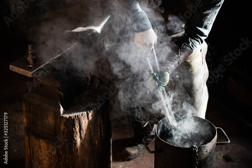 Blacksmith man putting a burning item in the bucket of water - steam coming out