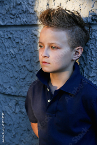 A handsome boy with a fashionable haircut is standing against a wall on the street. He is 13 years old. © IvSky