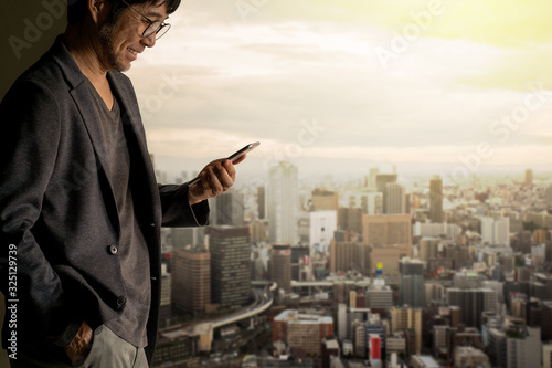 Asian businessman hand holding smartphone with blurred  cityscape