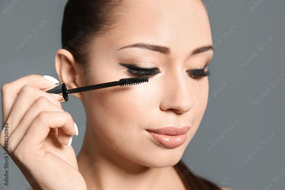 Beautiful woman applying mascara on light grey background, closeup. Stylish makeup