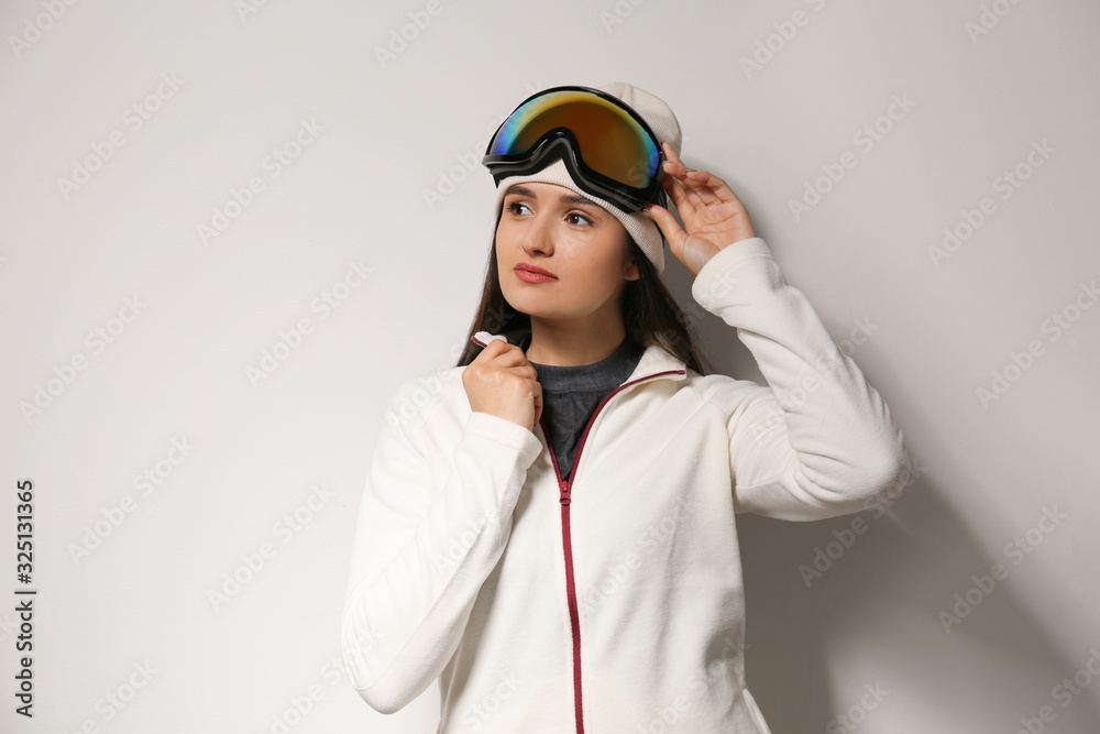 Woman wearing fleece jacket and goggles on light grey background. Winter sport clothes Woman wearing fleece jacket and goggles on light grey background. Winter sport clothes