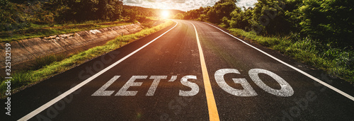 let's go written on highway road in the middle of empty asphalt road at  beautiful blue sky.