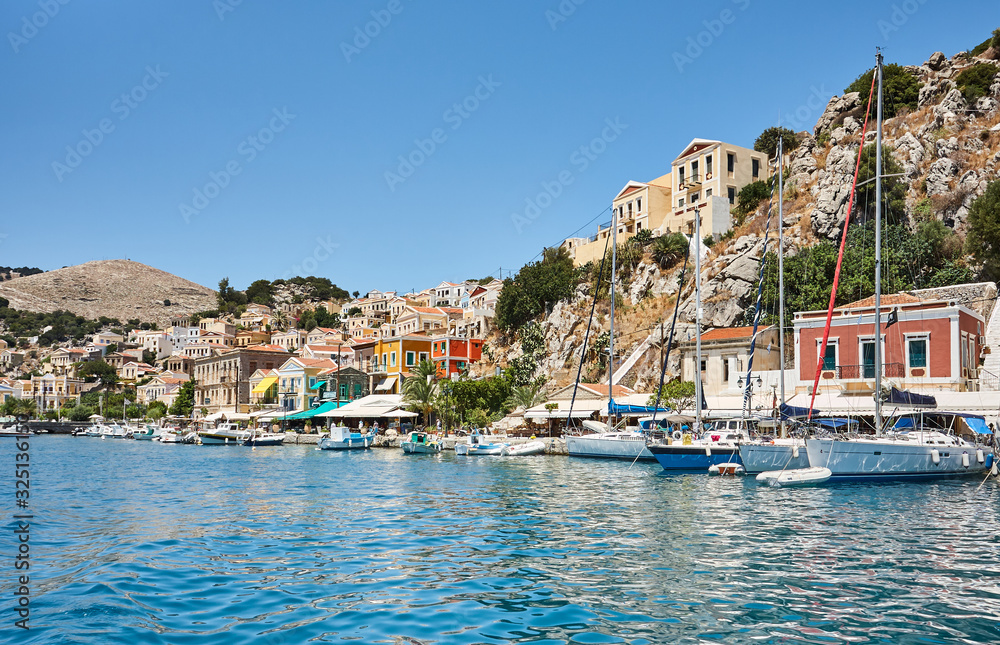 Symi port, Dodecanese islands, Greece, Europe; the picturesque waterfront line of Symi town with beautiful Greek houses and colorful buildings; small sailing yachts in harbor