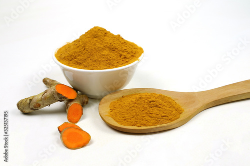 Turmeric powder in a white cup in a wooden spoon and isolated turmeric roots on a white background.Used as a tonic for the body and turmeric supplements or as an ingredient in food. Turmeric has anti-